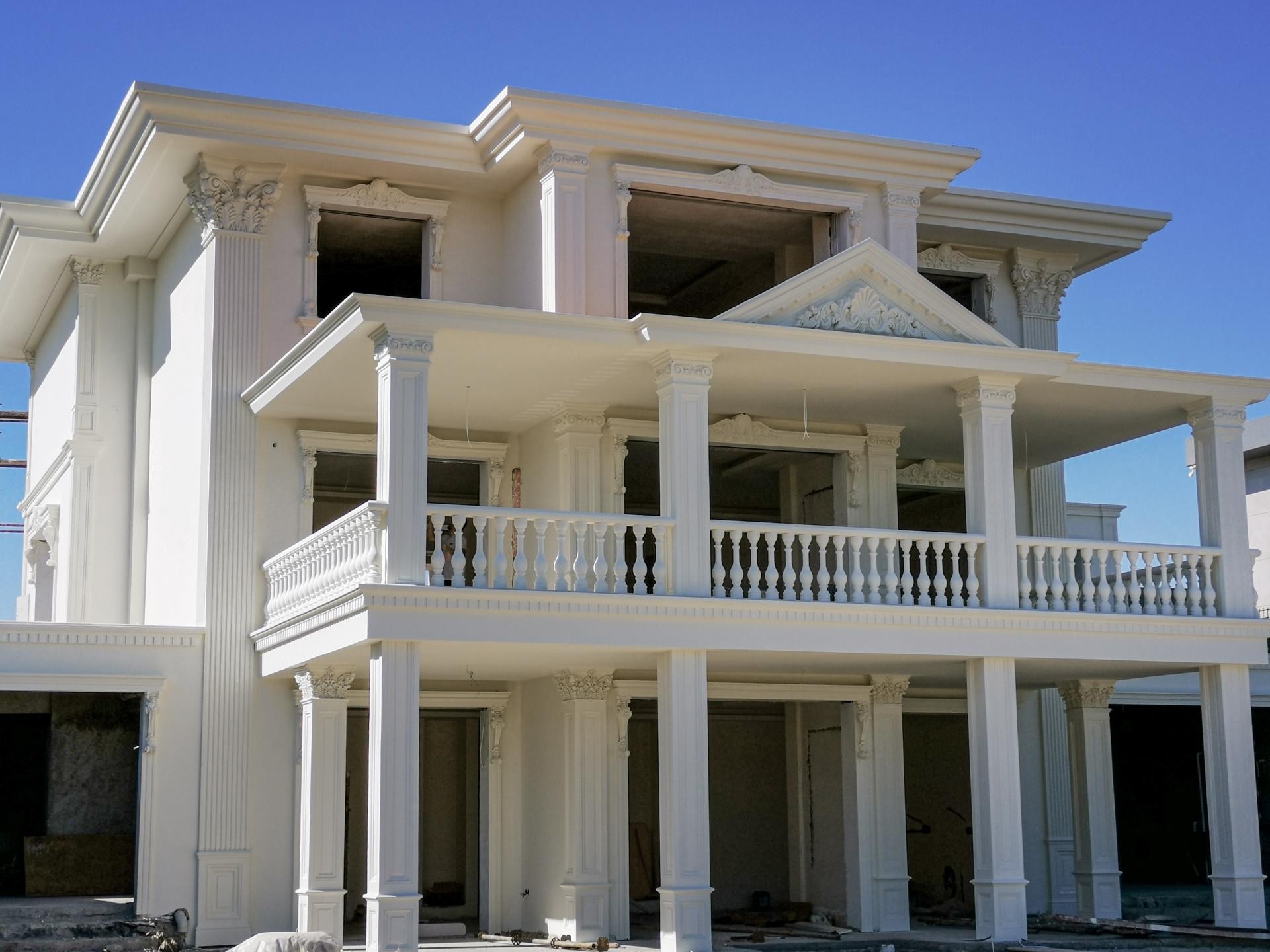 Fațadă albă de vilă clasică decorată cu pilatri din poliuretan, balustrade și fronton triunghiular pe balcon.