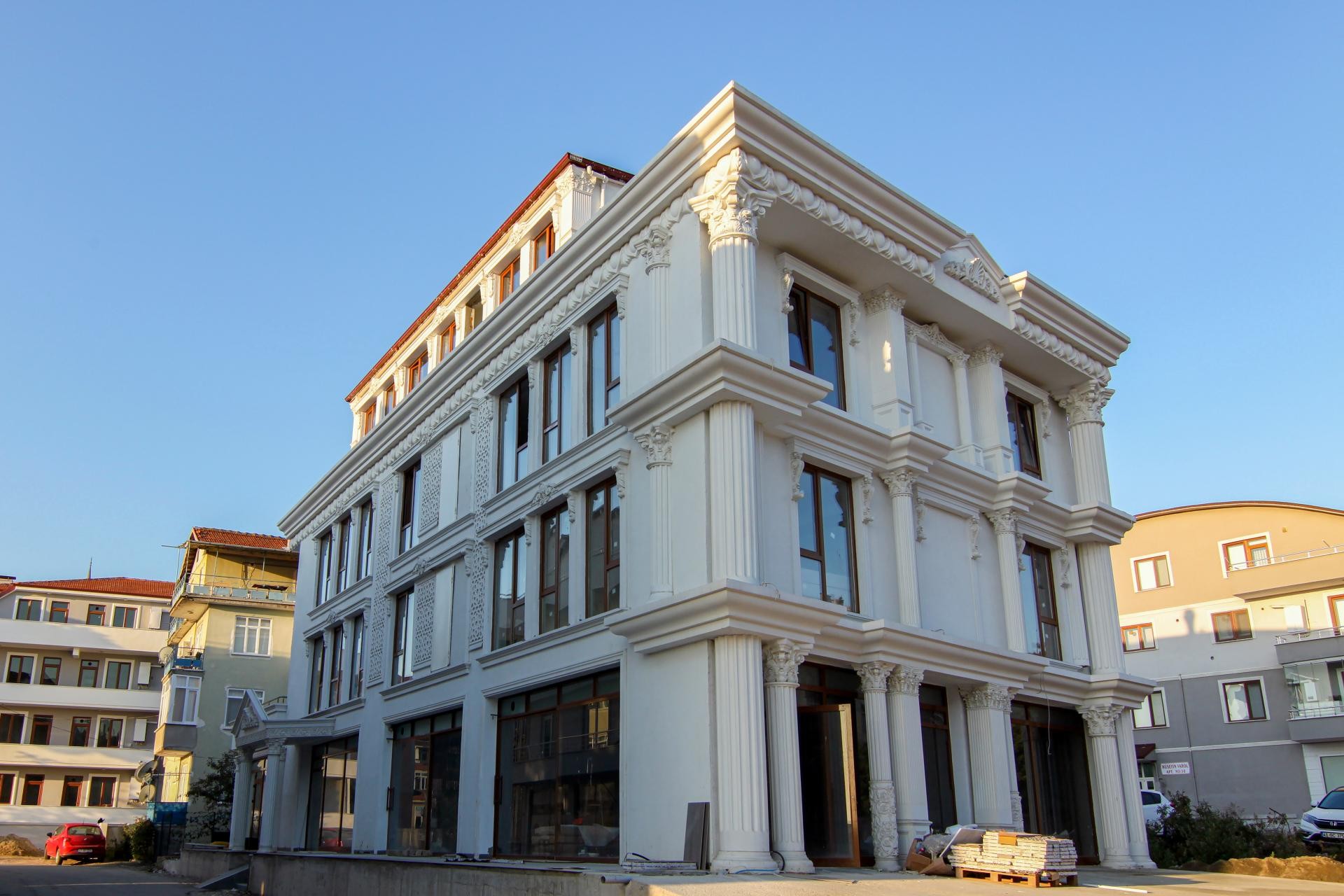 Fațadă albă din poliuretan cu coloane corintice, ancadramente decorative de ferestre și panouri ornamentale pe o clădire.