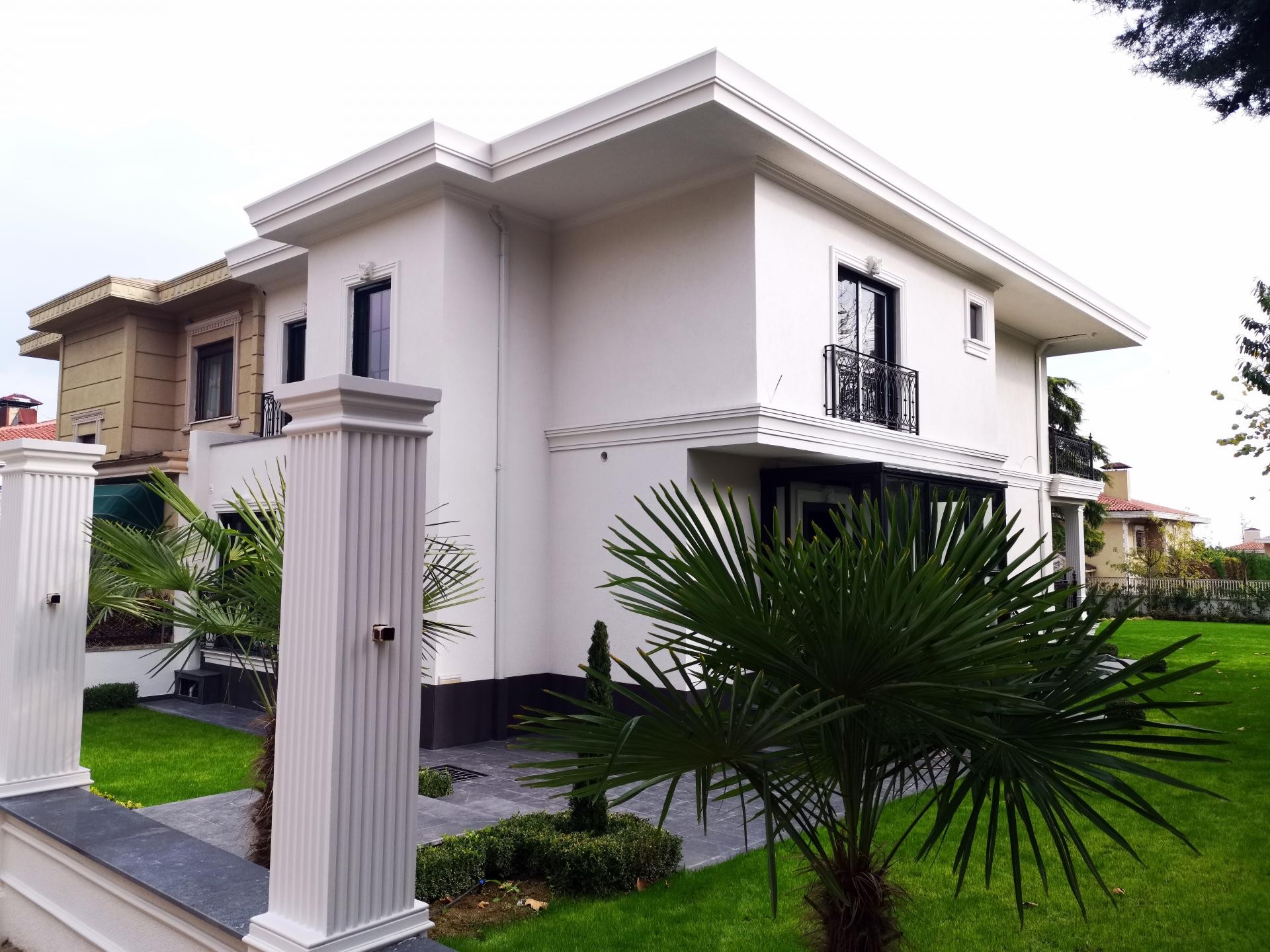 Fațadă de vilă albă modernă decorată cu pilaștri canelați din poliuretan P5030 și ancadramente negre la ferestre.