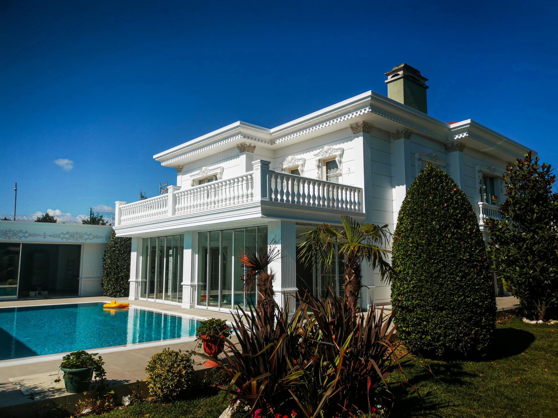 Fațadă albă de vilă clasică cu piscină, decorată cu pilastri, balustrade și profile din poliuretan.