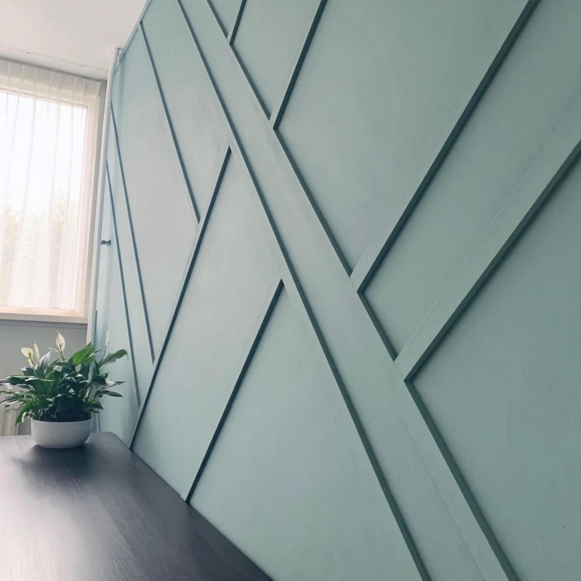 Perete verde decorat cu baghete din poliuretan în linii diagonale geometrice și birou din lemn închis