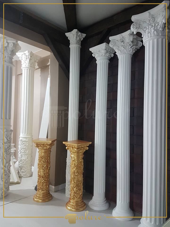 Coloane albe din poliuretan cu caneluri și pedestale aurii decorative pe fundal de cărămidă.