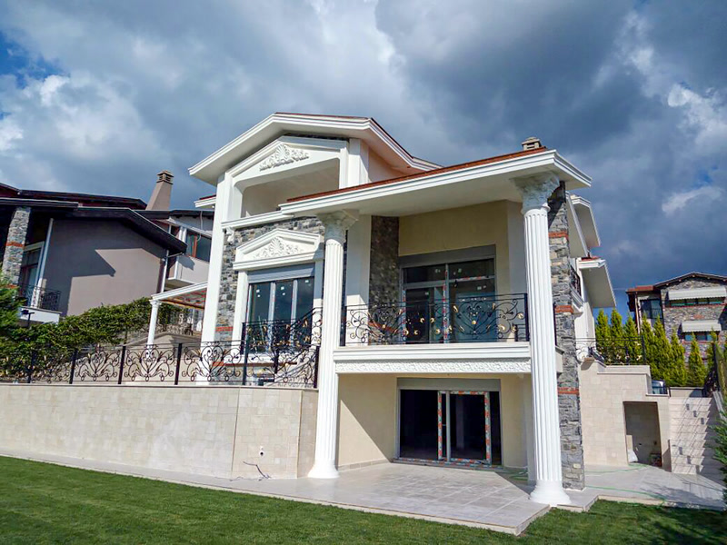 Fațadă exterioară de vilă clasică decorată cu coloane canelate din poliuretan, ancadramente de fereastră și frontoane decorative.