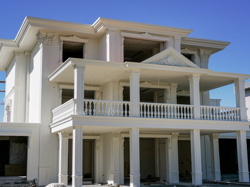 Fațadă albă de vilă clasică decorată cu pilatri din poliuretan, balustrade și fronton triunghiular pe balcon.