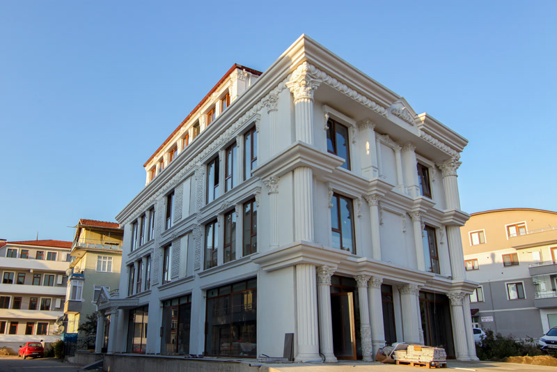 Fațadă albă din poliuretan cu coloane corintice, ancadramente decorative de ferestre și panouri ornamentale pe o clădire.