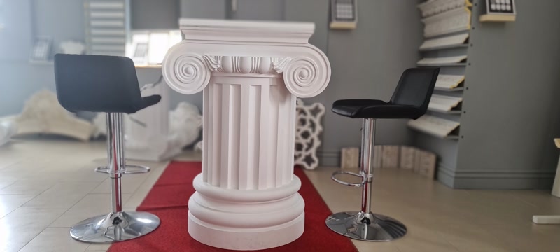 Coloană din poliuretan alb cu capitel ionic P5250I și fus canelat în spațiu expozițional modern cu scaune negre.