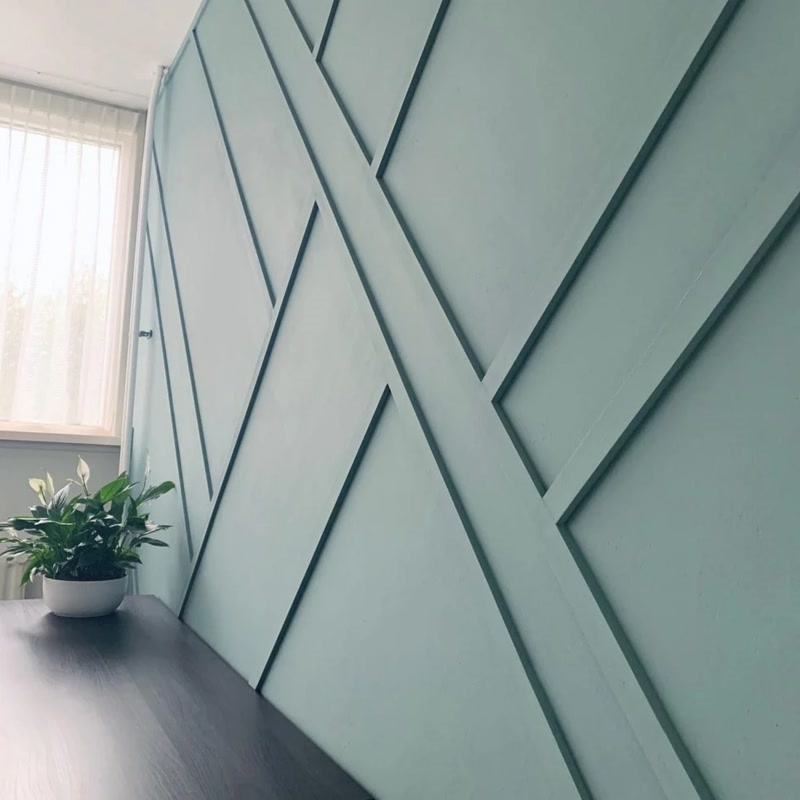 Perete verde decorat cu baghete din poliuretan în linii diagonale geometrice și birou din lemn închis