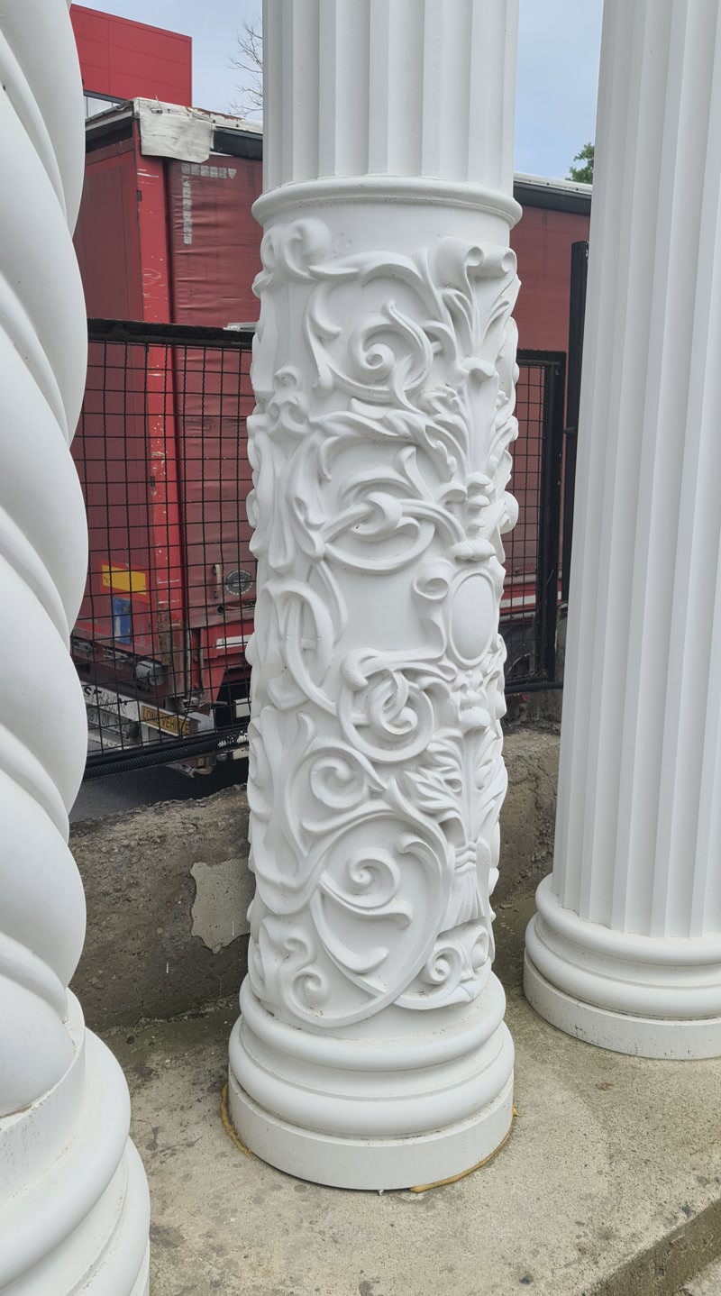 Coloană din poliuretan alb P5540 cu sculptură ornamentală bogată, amplasată lângă coloane canelate pe un suport din beton.