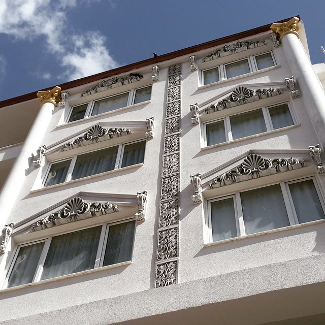 Fațadă albă de hotel cu ancadramente ferestre din poliuretan P2838, panouri verticale P8105 și piloni decorativi.
