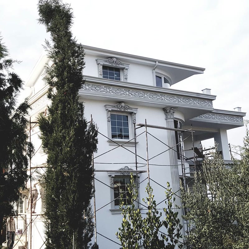 Fațadă de vilă albă în stil clasic cu ancadramente din poliuretan, coloane decorative și frontoane ferestre.