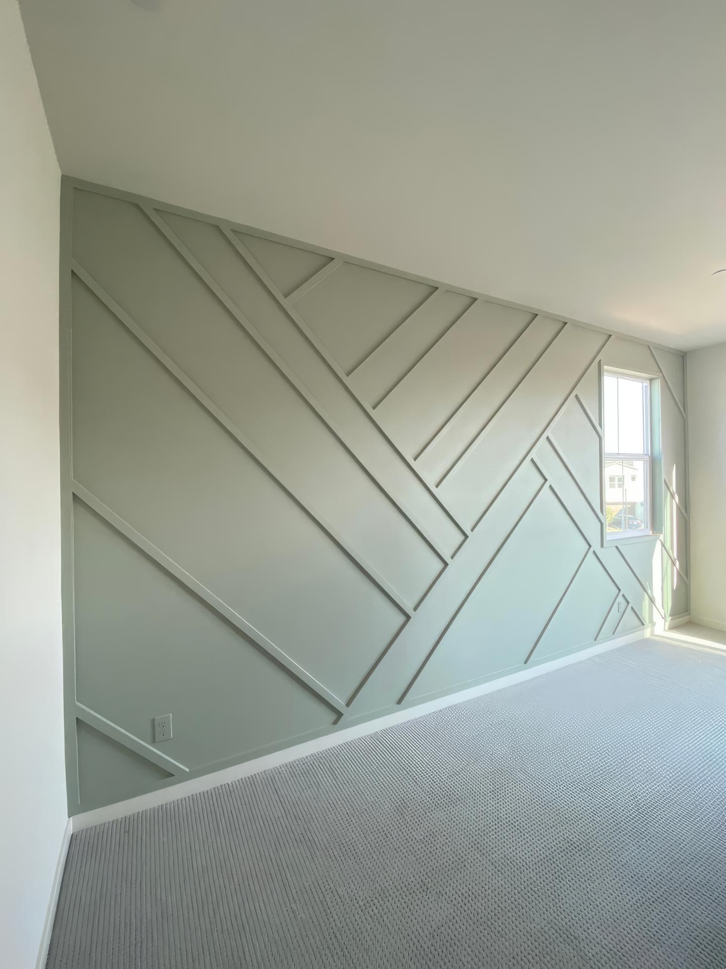 Perete accent verde salvie decorat cu profile din poliuretan în linii geometrice asimetrice într-o cameră modernă.