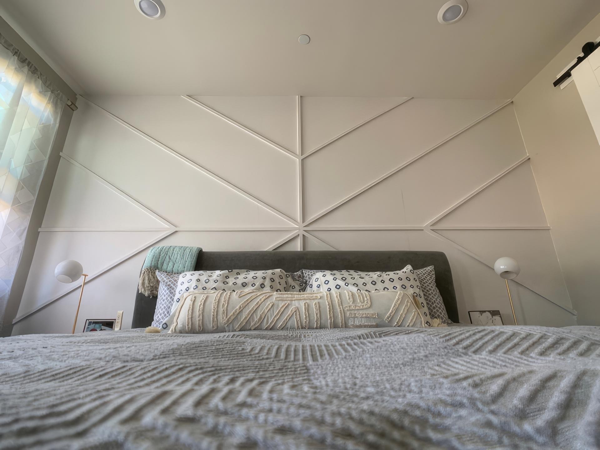 Perete de dormitor decorat cu profile din poliuretan în forme geometrice romboidale și tăblie de pat gri.