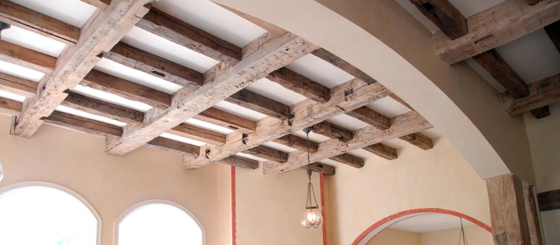 Tavan casetat decorativ cu grinzi din poliuretan aspect de lemn vechi si pereti de culoare calda intr-un salon rustic.
