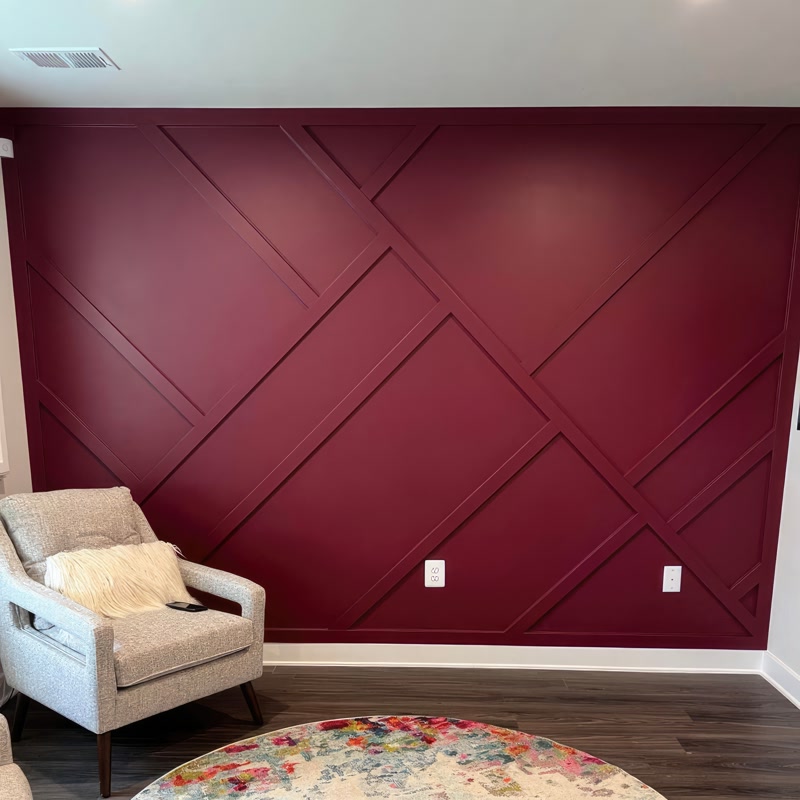 Perete accent bordo decorat cu profile din poliuretan P851350 în model geometric diagonal lângă un fotoliu gri.