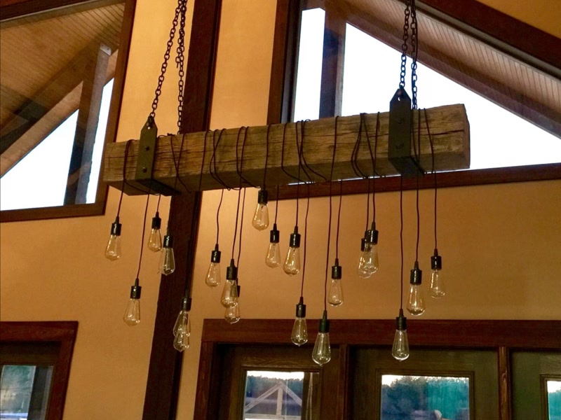 Lustră suspendată din grindă din poliuretan cu aspect de lemn rustic și becuri Edison pe lanțuri metalice.
