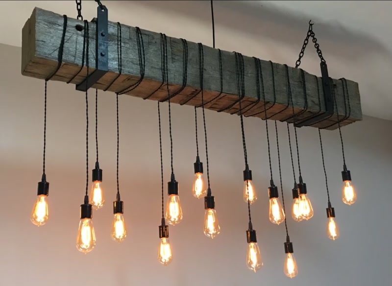 Lustră rustică realizată din grindă decorativă din poliuretan cu becuri Edison suspendate pe cabluri negre.