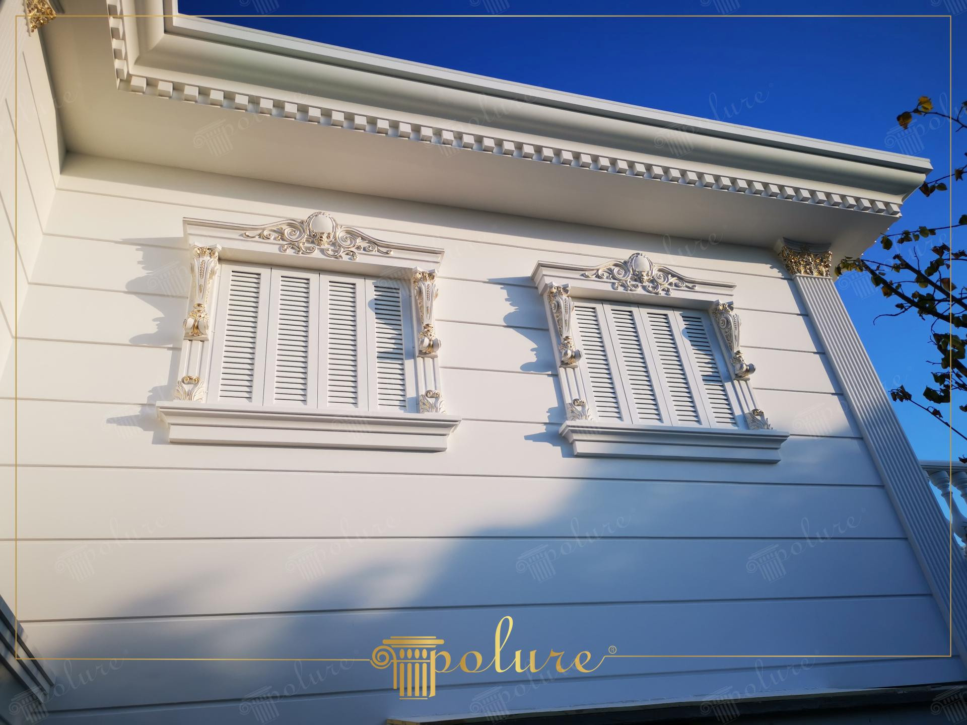 Ancadramente din poliuretan cu frontoane decorative și pilatri pe o fațadă albă de vilă cu ferestre și obloane