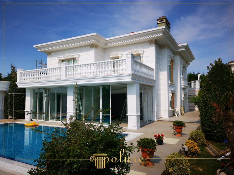 Fațadă albă de vilă cu pilastri din poliuretan, ancadramente la ferestre și balustradă la balcon lângă piscină.