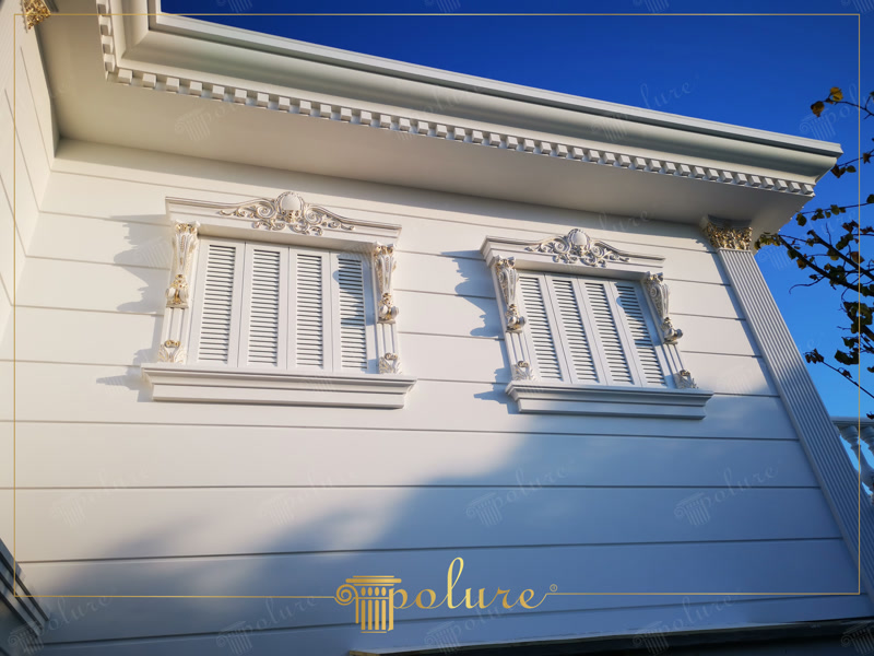 Ancadramente din poliuretan cu frontoane decorative și pilatri pe o fațadă albă de vilă cu ferestre și obloane