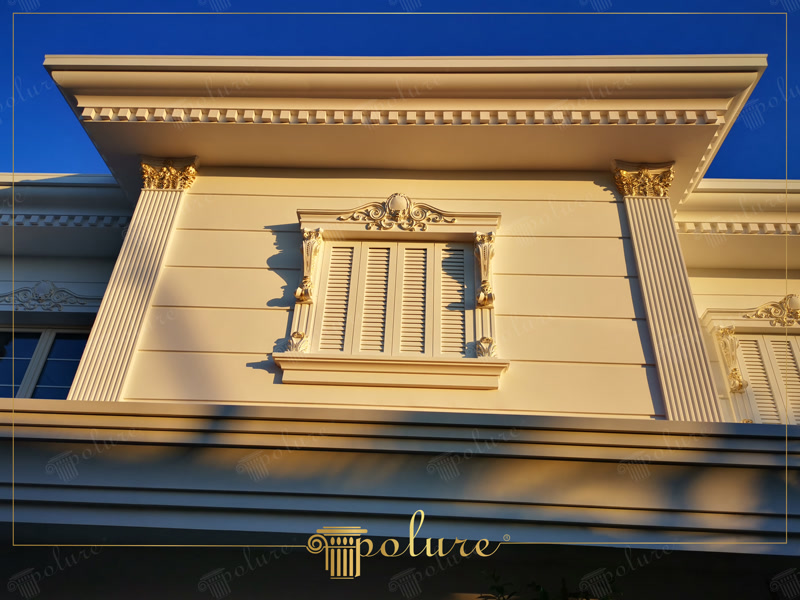 Ancadrament de fereastră din poliuretan cu fronton decorativ, pilaștri și detalii aurii pe fațada unei vile clasice.