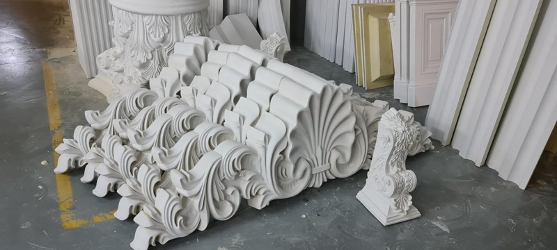 Frontoane și ornamente din poliuretan alb P2838 suprapuse într-un atelier, alături de console decorative sculptate.