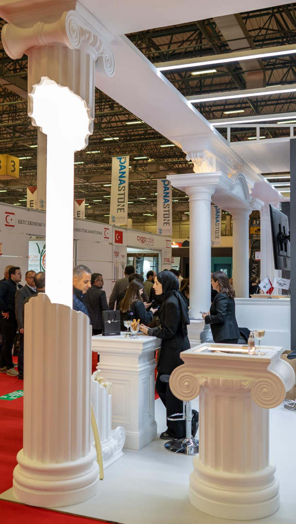 Stand expozițional amenajat cu coloane din poliuretan canelate, capiteluri ionice albe și mese moderne.