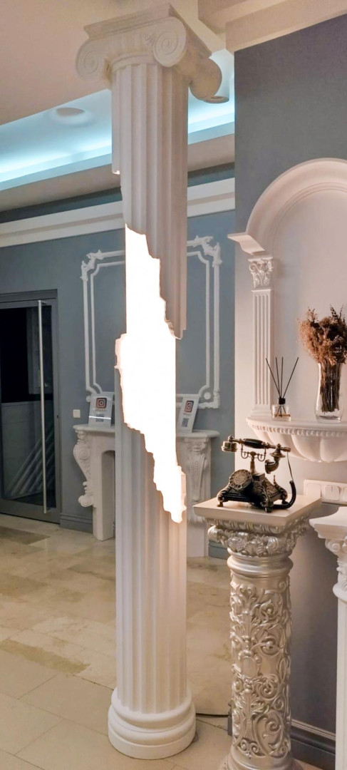 Coloană din poliuretan cu capitul ionic și iluminat LED integrat pe fundal cu perete gri și profile decorative.