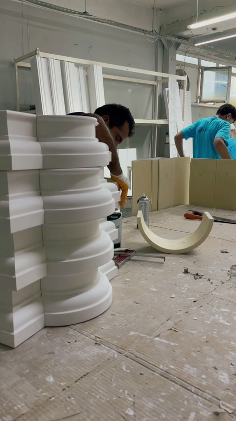 Atelierul prezintă un muncitor prelucrând profile curbate lângă elemente stivuite.