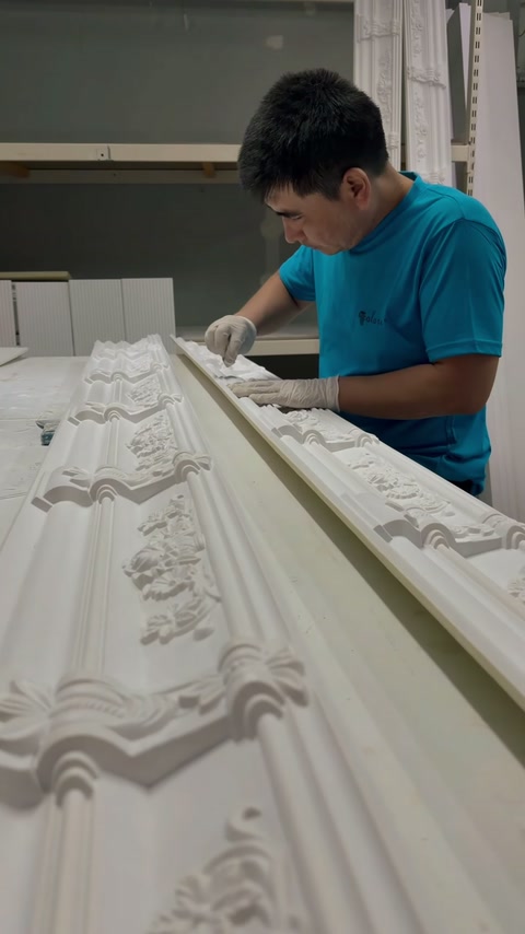 Un artizan curăță detaliile reliefate ale unei cornișe ornamentale lungi.