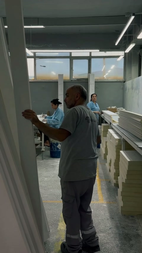 Un lucrător inspectează un profil decorativ lung în secția de finisare.