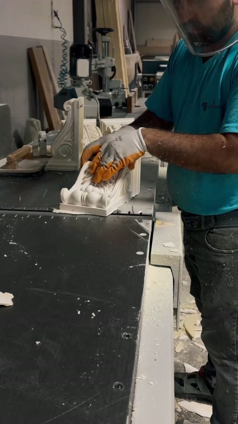 Operatorul prelucrează mecanic o consolă ornamentală pe bancul din atelier.