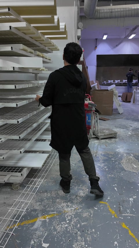 Bărbat trece prin atelier pe lângă rafturi cu profile