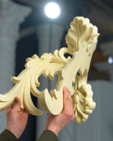 Mâini țin o consolă ornamentală lângă coloane decorative.