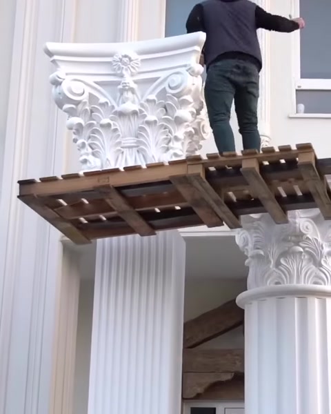 Muncitor pe schelă ajustează capitelul unui stâlp canelat