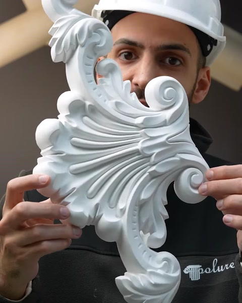 Tânăr muncitor ține un ornament decorativ alb din poliuretan.
