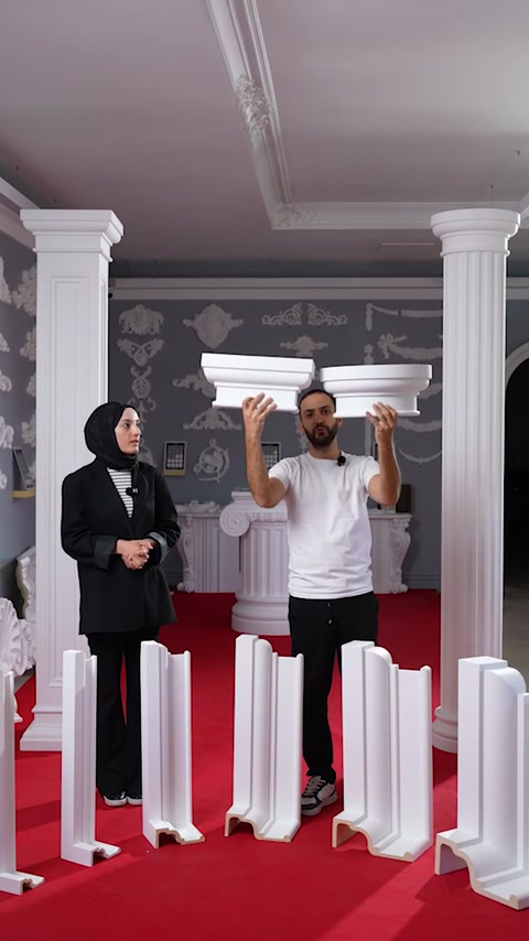 Prezentatorii compară două capiteluri decorative între coloane expuse în showroom