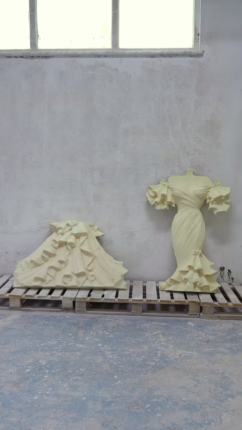 Componentele sculptate ale rochiei sunt așezate lângă peretele atelierului.