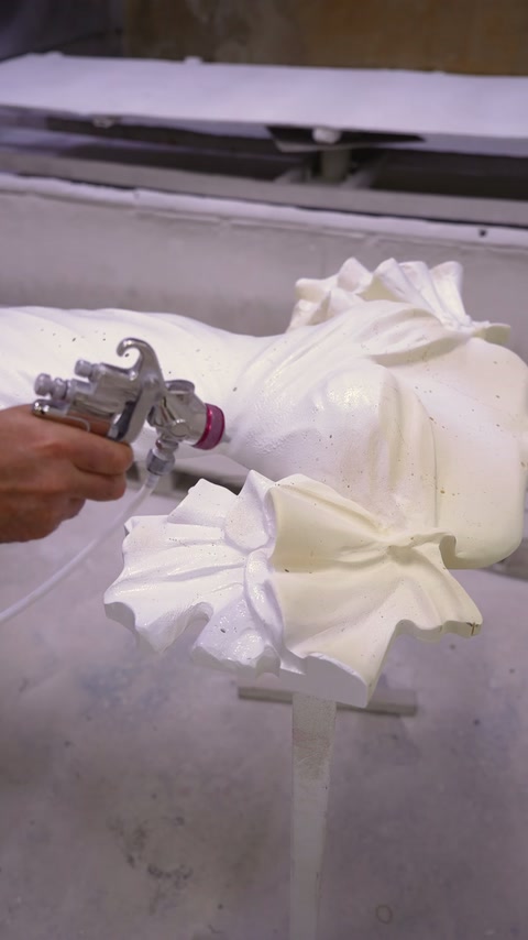 Pistolul pulverizează stratul alb peste pliurile reliefului de rochie.