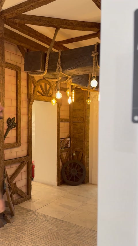 Ansamblu rustic de grinzi încadrează intrarea și corpurile de iluminat suspendate.