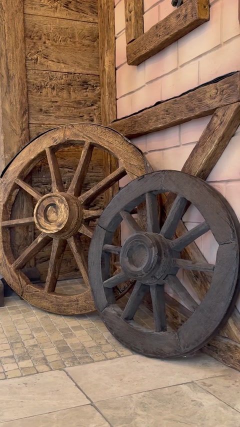 Grinzi cu aspect antichizat și roți decorative completează peretele rustic.