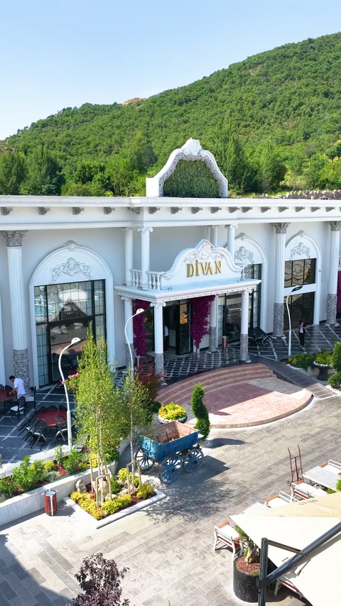 Perspectiva panoramică arată intrarea decorată, terasa și peisajul montan.
