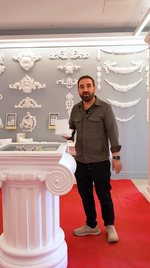 Prezentatorul arată o consolă mică în fața panoului decorativ