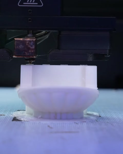 Imprimantă 3D în funcțiune, realizând o piesă decorativă din rășină albă.
