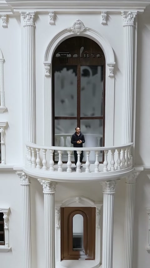 Fațada miniaturală arată un balcon curbat, coloane și fereastră arcuită.
