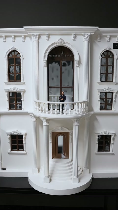 Clădirea miniaturală include ferestre, balcon, coloane și trepte curbate.