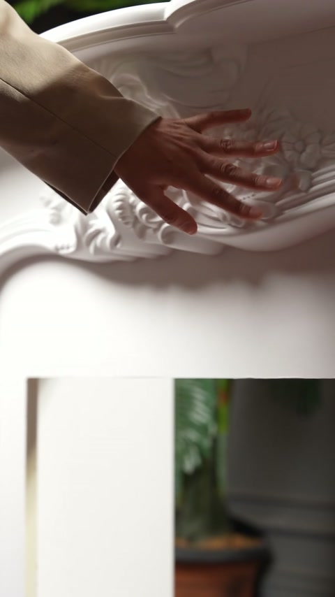 Mâna parcurge decorul sculptural alb, evidențiind frunzele și curbele ornamentale.