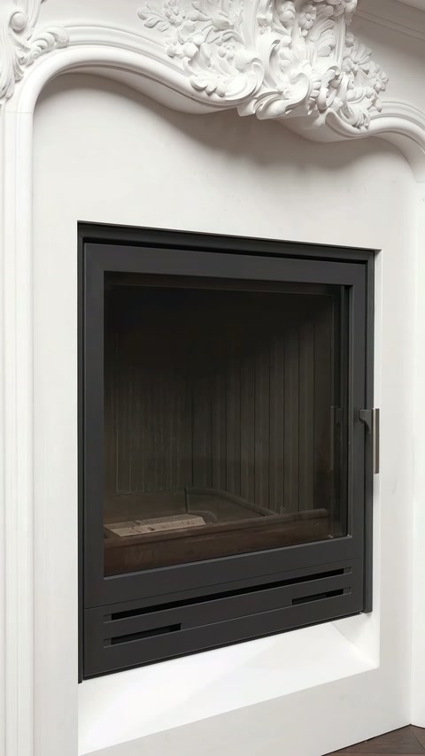 Șemineul negru apare montat într-o ramă albă cu arc ornamental.