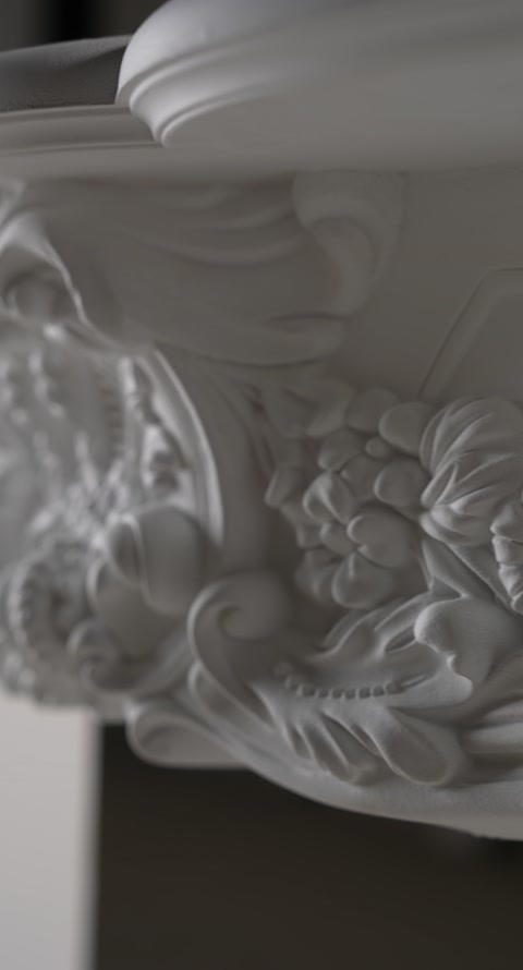 Ornament floral central sculptat sub polița albă a șemineului.