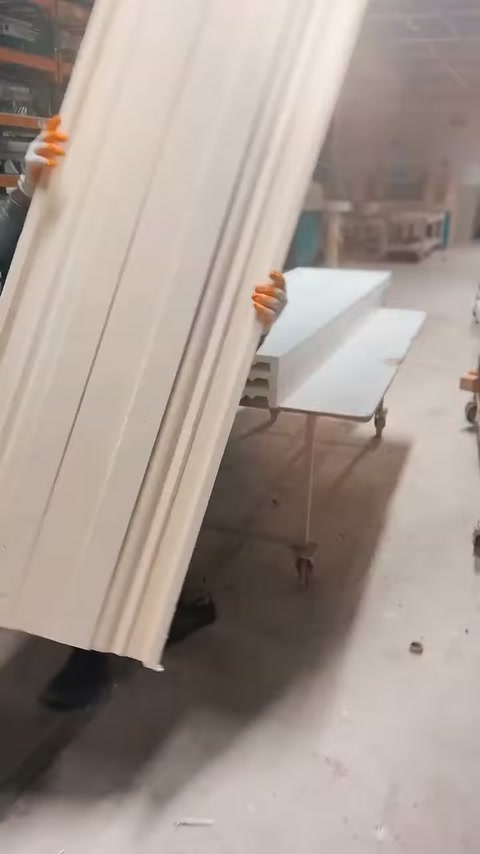 Muncitorul transportă vertical mai multe profile albe prin atelier.
