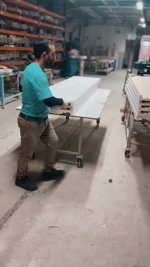 Muncitorul rotește un element decorativ voluminos lângă căruciorul metalic.
